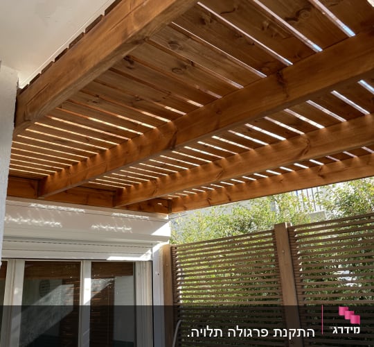 פרגולה מעץ מעל חלון עם תריסים מעץ